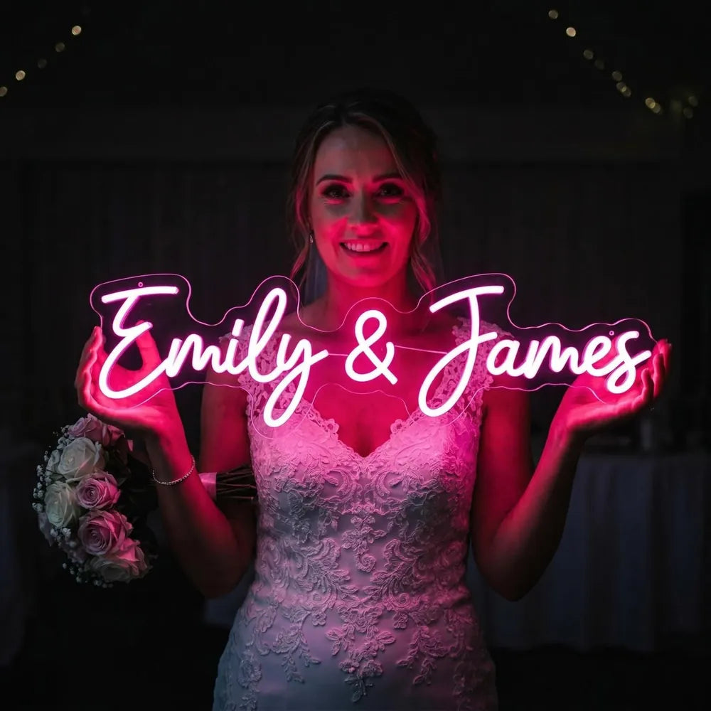Braut hält ein pinkes Neonschild mit den Namen Emily und James